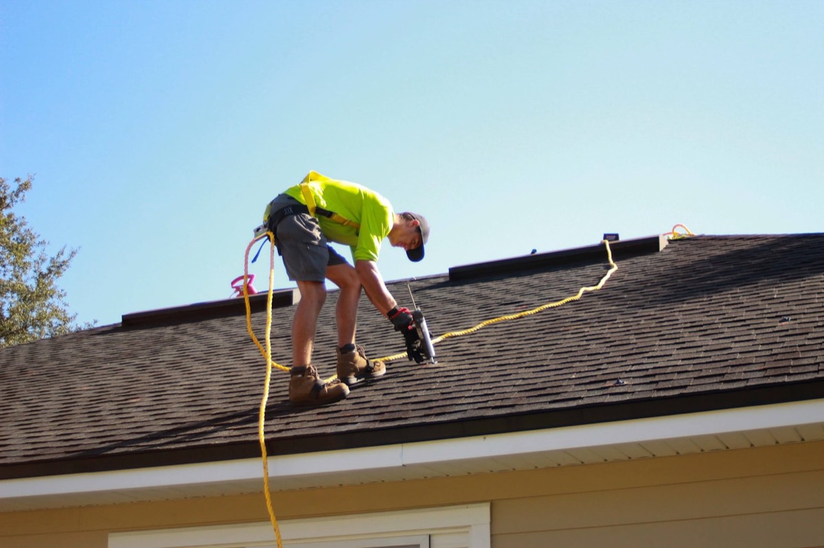 Roofer nailing new asphalt shingles by hand